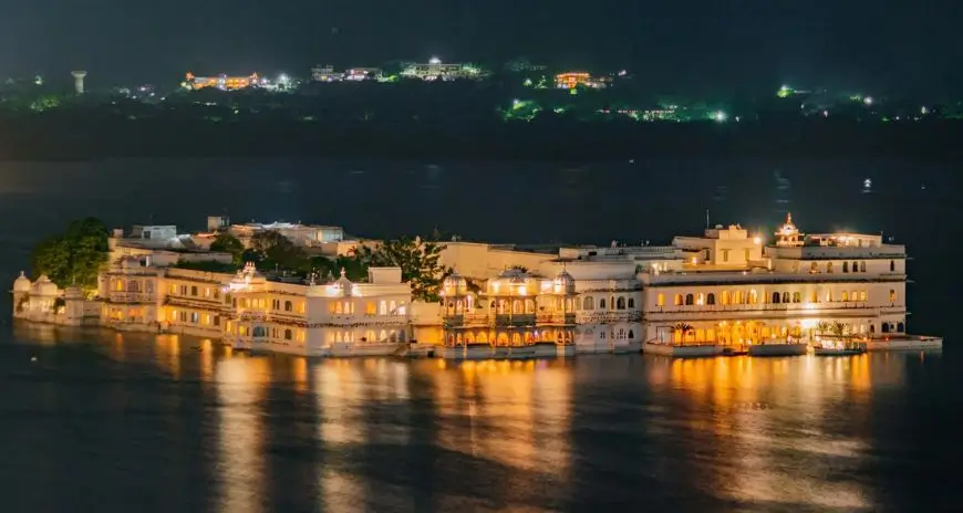 Udaipur City Palace illuminated at night beside Lake Pichola